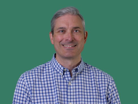 Man in blue checked shirt standing against green background